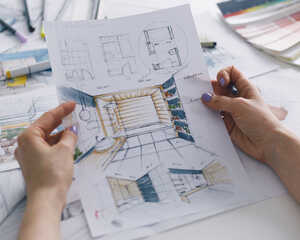 Person holding design sketches with color samples and tools on a workspace.